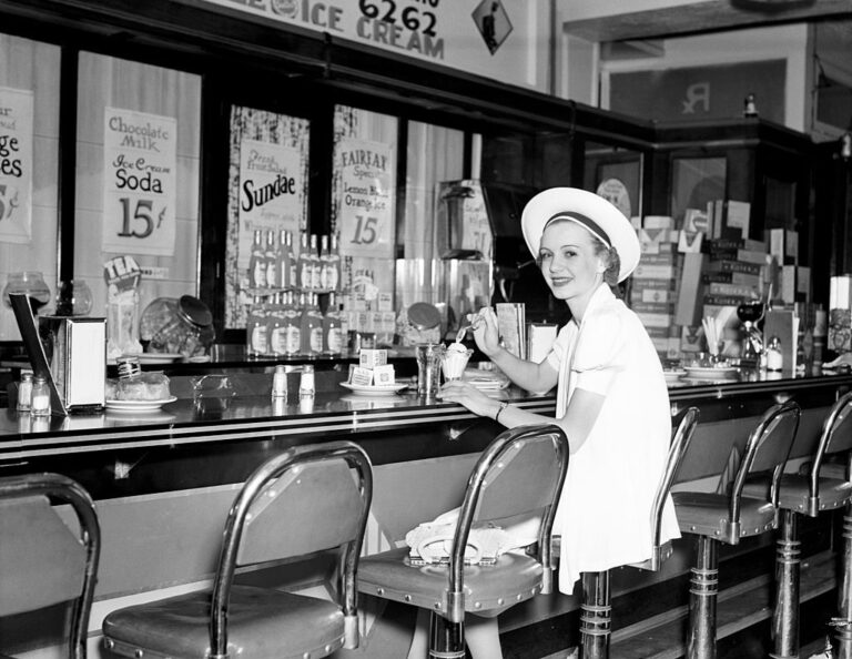 Woman in white dress hat sitting at soda fountain